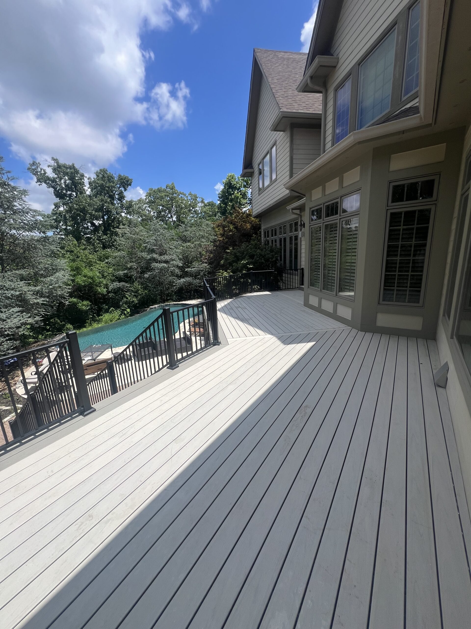 Spacious deck overlooking pool and lush trees.
